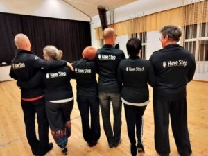 Miehiä ja naisia kuvassa selin, päällä takki jonk selässä seuran nimi.