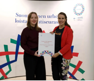 Kaksi naista seisoo katsoen kameraan ja pitävät yhdessä kunniakirjaa.