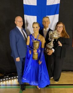 Suomenlipun edessä nuori voittajapari ja heidän valmentajat.