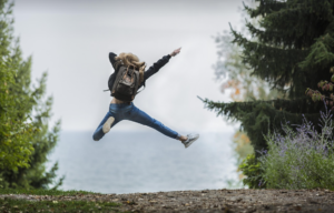 Nainen reppu selässä hyppää ilmaan.