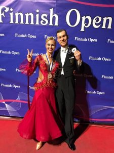 Luca Rossignoli ja Merje Styf hymyilevät iloisesti Finnish Openin mitalit kaulassa. Merje näyttää sormillaan voitonmerkkiä.