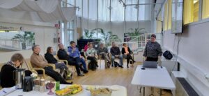 Miehiä ja naisia istuu kuuntelemassa esitelmöijää.