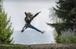 Nainen reppu selässä hyppää ilmaan.